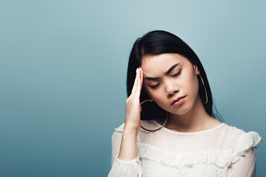 Upset Brunette Asian Woman With Headache On Blue Background