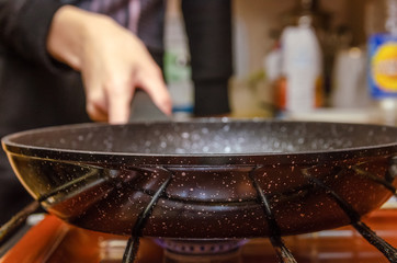 Home cooking. Woman holding a frying pan by the handle of the stove close-up.