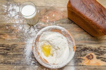 Fresh bread brick on the table closeup. Next is a bowl of flour and egg, a glass of milk. view from the top