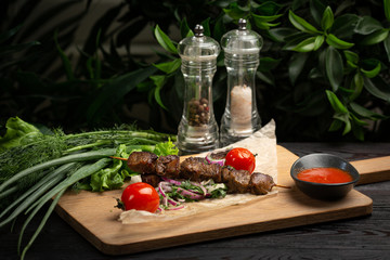 lamb skewers with pickled onions and cilantro on a wooden board decorated with leafy greens