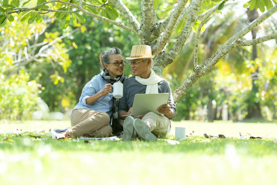 Asian Lifestyle senior elderly retire couple drinking coffee and working online  in the nature park happy and relax time.  Elderly family the rest and chill  after retirement in vacations.