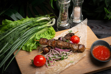lamb skewers with pickled onions and cilantro on a wooden board decorated with leafy greens
