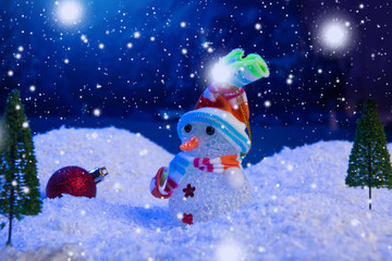 Snowman with Christmas balls on snow over fir-tree, night sky and moon. Shallow depth of field. Christmas background. Fairy tale. Macro. Artificial magic dreamy world.
