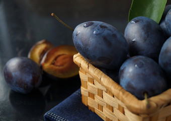 Fresh juicy plums in basket on black metal background with reflection