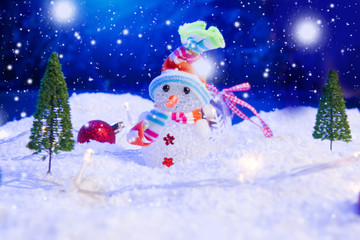 Snowman with Christmas balls on snow over fir-tree, night sky and moon. Shallow depth of field. Christmas background. Fairy tale. Macro. Artificial magic dreamy world.
