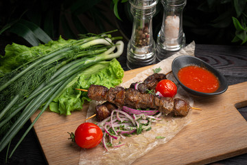 lamb skewers with pickled onions and cilantro on a wooden board decorated with leafy greens