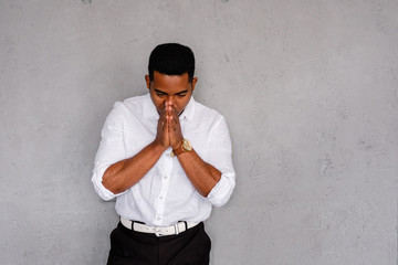 Young desperate ethnic young male businessman praying bowing his head and posing on a gray background. Concept of failures and black stripe in life. Advertising space