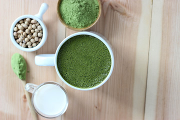 Top view, Closes up Hot Green Tea Matcha Latte on smooth brown wooden board. Decorate with powder extract and soy beans, milk.