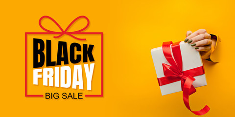 Hands holding gift box with black friday lettering on yellow background. Concept of sales, black...