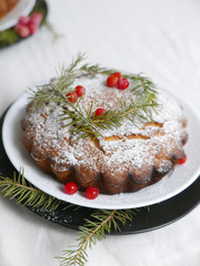 Fototapeta na wymiar traditional christmas cake decorated with berries, icing sugar and green sprigs on a white table
