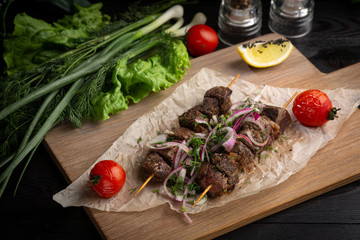 beef skewers with pickled onions and cilantro on a wooden board decorated with leafy greens