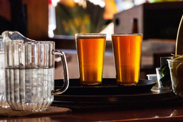 Two glasses of cold, amber beer wait to be served in a bar.