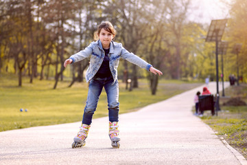 Cute little girl rides inline skating rollerblades in the park