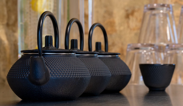 Close up of black textured cast iron Asian style tea pots with handles and matching cups.