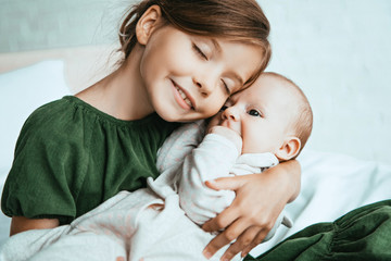 adorable child smiling with closed eyes while holding little sister