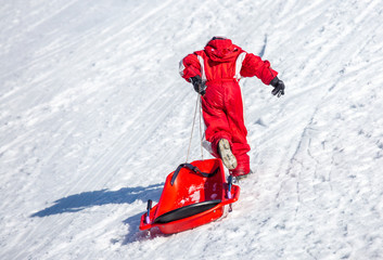 Fototapeta na wymiar Unrecognizable kid pulling sled on slope