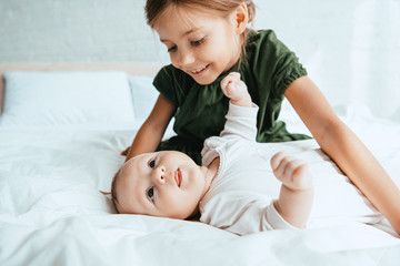smiling child looking at adorable infant lying on white bedding