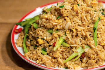 Fried rice mix with egg and vegetable in white and red dish on wooden table.