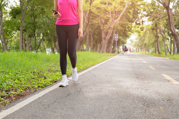 Fitness woman exercise walking on park trail with hand holding cell phone.