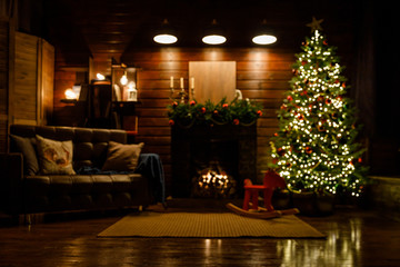 Christmas and New Year interior - blur background: fireplace, lamps, green Christmas tree, brown leather sofa, gifts, candles, moose rocking chair.  Lots of lights glowing in the dark.