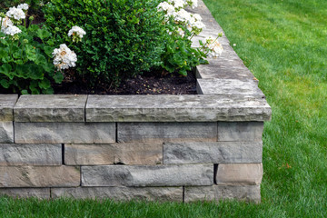 A natural stone retaining wall with matching coping creates a raised planter bed which has been...