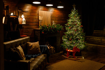 Christmas and New Year interior: fireplace, lamps, green Christmas tree, brown leather sofa, gifts, candles, moose rocking chair.  Lots of lights glowing in the dark.