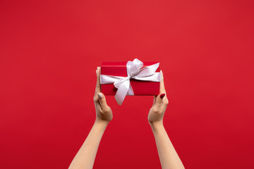 cropped view of woman holding wrapped Christmas present with white ribbon isolated on red background. Christmas concept