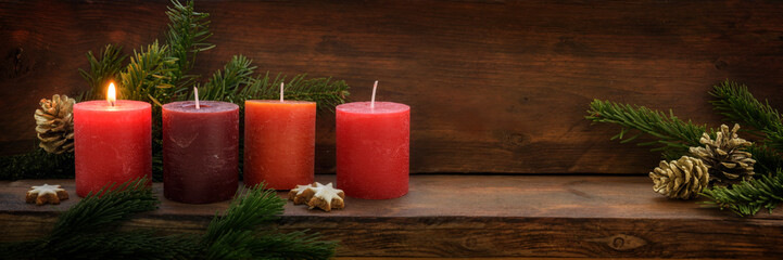 First Advent, four red candles, one of them is burning, fir branches and Christmas decoration on...