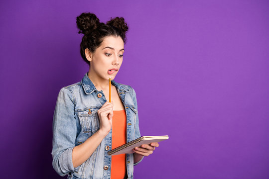 Turned photo of astonished girl hold copybook want write note review in book have project problem think hesitate bite teeth lips wear jeans clothes isolated copyspace violet purple color background