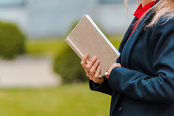 cropped view of businesswoman in black coat holding book