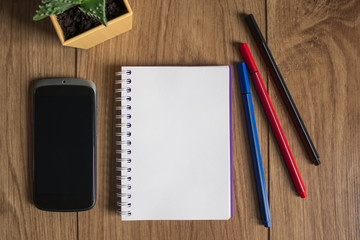A notebook for writing lies on the table. Office tools. Set of pens, phone, paper and flowers. Space for recording. White background. Copyspace.