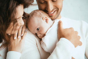 cropped view of happy man holding adorable baby near smiling wife - Powered by Adobe