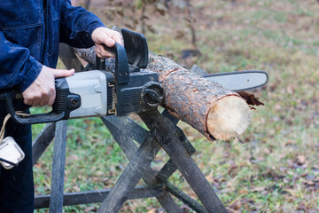 A man in blue uniform cuts pine wood with an electric saw. Horizontal photo