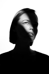 Fototapeta premium Fashionable beauty portrait. Black silhouette on white background. Girl with a spot of light on her face. 