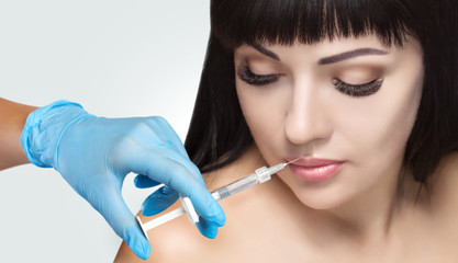 The doctor cosmetologist makes Lip augmentation procedure of a beautiful woman in a beauty...