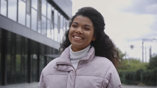 smiling african american woman in puffer jacket walking on street