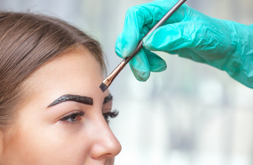 The make-up artist applies a paints eyebrow dye on the eyebrows of a young girl. Professional make-up and face care.