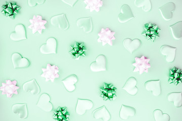 Beautiful silk hearts, white and green holiday bows on a green background, pastel colors . Celebrate concept. Flat lay .