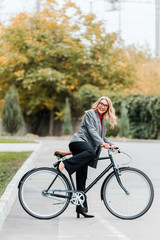 attractive businesswoman in coat and glasses smiling and riding bike
