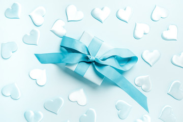 Gift box of pink color with a large bow from a blue ribbon on a blue background decorated with silk hearts. Holiday concept.