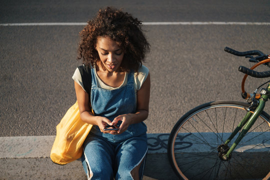 Woman sit outdoors with bicycle using mobile phone.