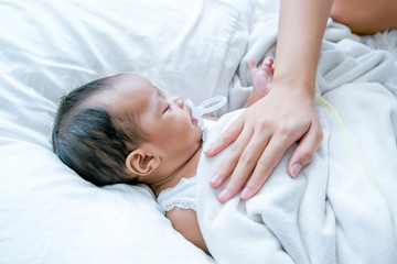 Fototapeta na wymiar Asian newborn baby is sleeping on white bed with mother hand put on her chest to take care and make her feel safe.