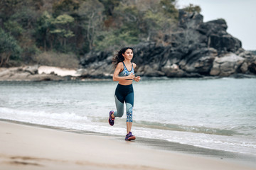 Active healthy lady is jogging across the sandy beach near the Andaman sea.