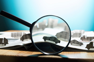 Magnifying glass in front of an open newspaper with paper cars. Concept of car rent, search,...