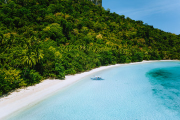 Aerial view of tropical boat moored at secluded white sand beach with turquoise ocean lagoon...