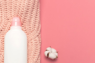 Obraz na płótnie Canvas Eco cleaning concept. White plastic packaging of laundry detergent, liquid powder, washing conditioner, knitted wool sweater, cotton flowers on pink background. Flat lay top view. Bio organic product
