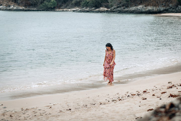 A pensive young lady walks alone the beach alone, looking down at the wet sand and the sea.