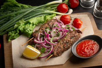 lula kebab of beef on skewers with onions, greens, ketchup and lemon on a board