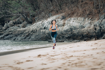 A happy  slim girl iruns across the sandy beach near the water in Vietnam. Rocks and trees behind.