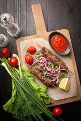 lula kebab of beef on skewers with onions, greens, ketchup and lemon on a board